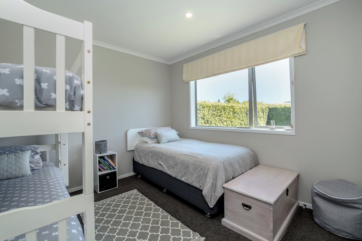 A bedroom with bunk beds, a single bed, a window with a view, and a small bedside table.