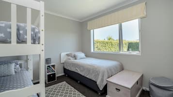 A bedroom with bunk beds, a single bed, a window with a view, and a small bedside table.
