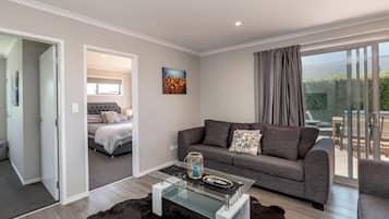 A modern living room with a glass coffee table, grey sofa, and a view of a balcony.