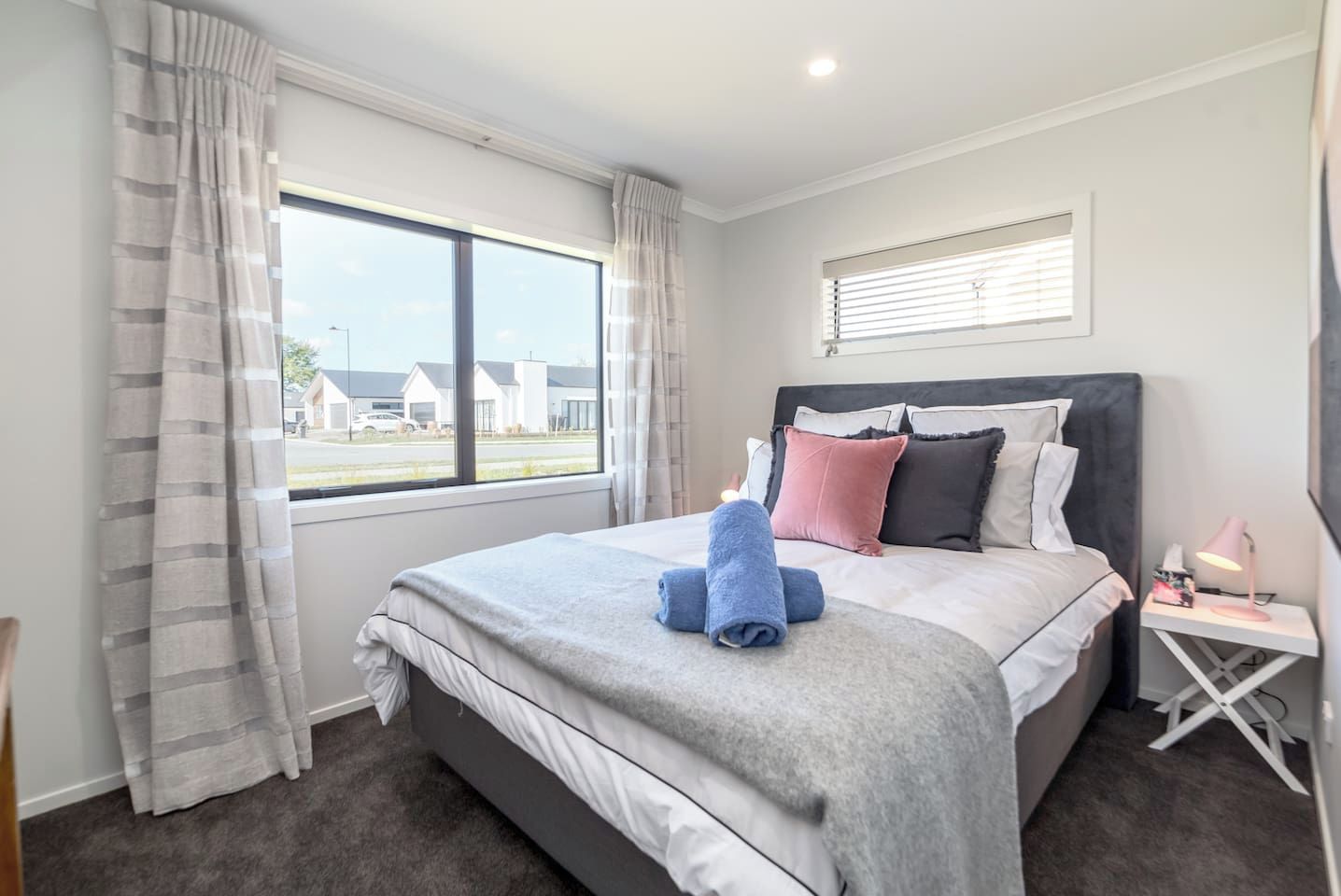 Una habitación de hotel con una cama grande, una mesita de noche con lámpara y una ventana con cortinas.
