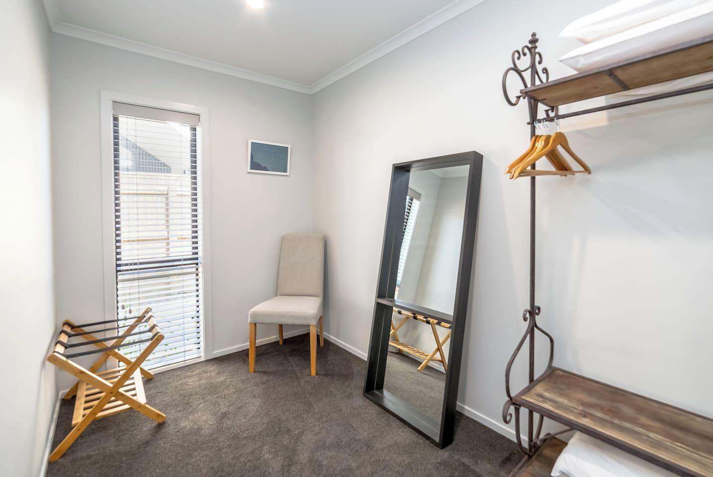 A room with a large mirror, a chair, a wooden drying rack, and a coat rack.