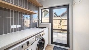 Eine kompakte Küche mit Waschmaschine, Spüle und Fenster mit Blick auf eine Holzterrasse.