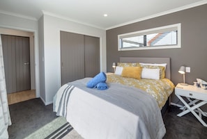 Een slaapkamer met een bed, nachtkastje, lamp en een raam met jaloezieën.
