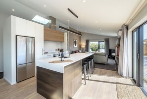A modern kitchen with a central island, stainless steel appliances, and a dining area with a sofa and TV. - Citron 9, Greytown, Wairarapa (Greytown)