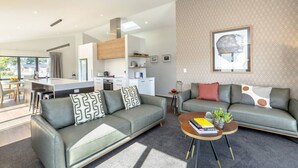 Ein modernes Wohnzimmer mit einem grauen Sofa, einem Couchtisch und einer Küche im Hintergrund.