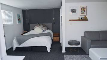 A bedroom with a bed, bedside tables, a grey sofa, a small stool, and artwork on the wall.