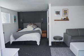 A bedroom with a bed, bedside tables, a grey sofa, a small stool, and artwork on the wall.