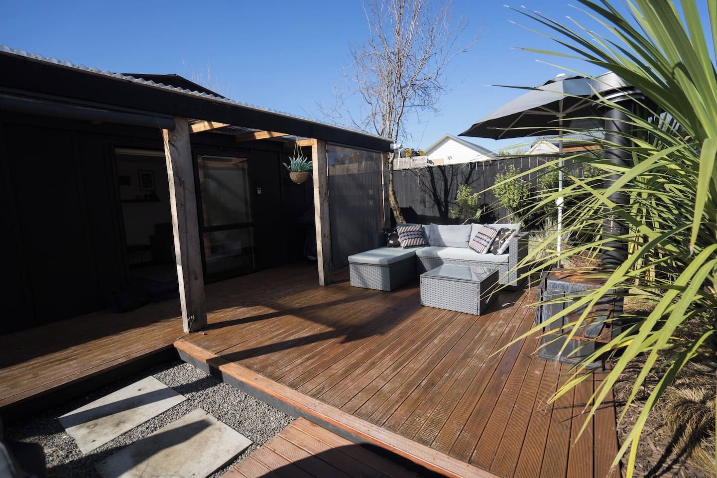 Une terrasse en bois avec des meubles d’extérieur, un espace salon couvert et une vue sur un bâtiment en arrière-plan.