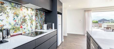 Una cocina moderna con una isla grande, muebles oscuros y un mural tropical llamativo.