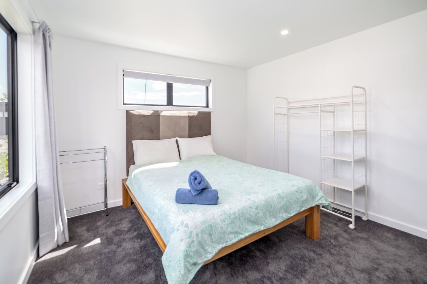 Ein Hotelzimmer mit Bett, Fenster, Heizkörper und einer weißen Metallregaleinheit.