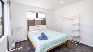 Ein Hotelzimmer mit Bett, Fenster, Heizkörper und einer weißen Metallregaleinheit.