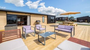 An outdoor patio area with wooden flooring, modern furniture, and a barbecue grill. - 53 Burgundy – Large Group Retreat with Seasonal Communal Pool, Tennis & Expansive Deck (Martinborough)