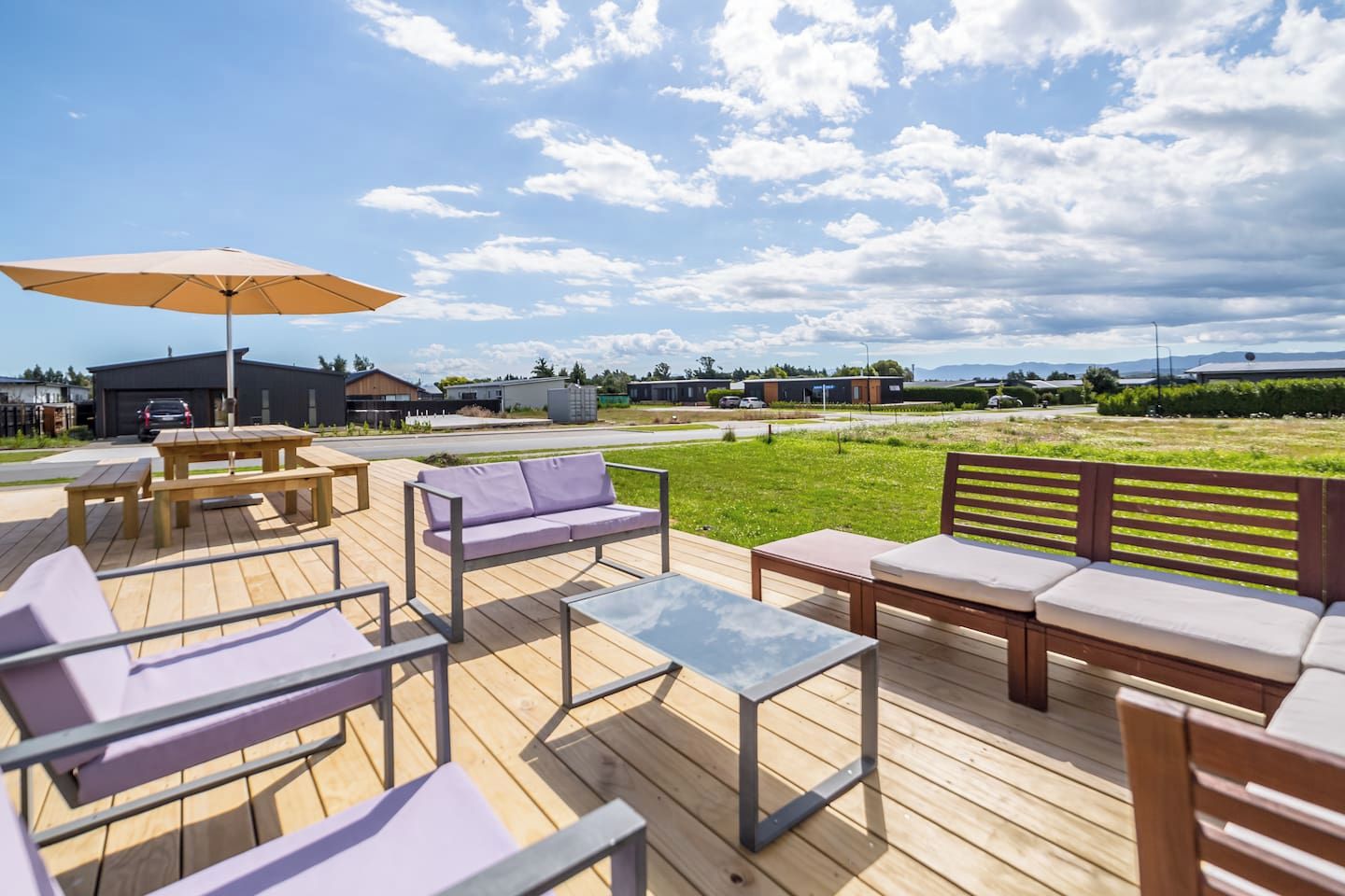 An outdoor deck with wooden furniture, including a sofa, chairs, and tables, under a large umbrella.