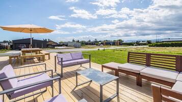 An outdoor deck with wooden furniture, including a sofa, chairs, and tables, under a large umbrella.
