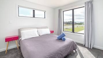 A bedroom with a bed, a nightstand, a window with curtains, and a view of the outdoors.