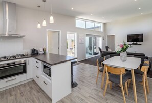 Eine moderne Küche mit Kochinsel, ein Essbereich mit Tisch und Stühlen sowie ein Wohnbereich mit Sofa und Fernseher.