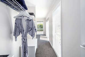 A hallway with a white wall, a hanging rack with patterned clothing, a white door, and a window with blinds.