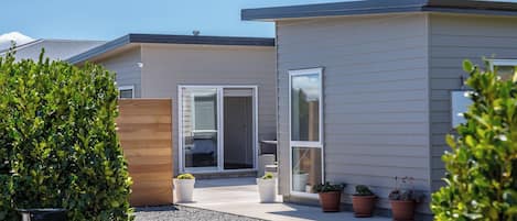 A modern two-story house with a covered patio, a sliding glass door entrance, and potted plants.