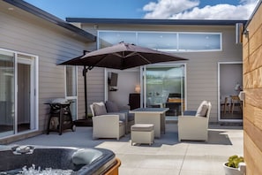 A modern outdoor patio with a hot tub, wicker furniture, and a large umbrella.