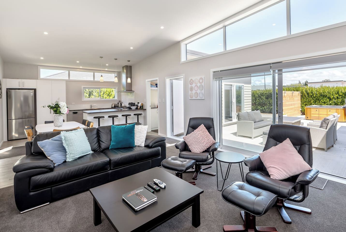 A modern living room with a black leather sofa, a coffee table, and a dining area with a white table and bar stools.