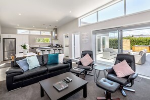 Ein modernes Wohnzimmer mit einem schwarzen Ledersofa, einem Couchtisch und einem Essbereich mit einem weißen Tisch und Barhocker.