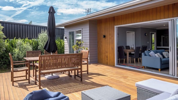 A modern outdoor patio with wooden furniture, a covered seating area, and a view into the adjacent living space.