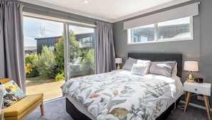 A bedroom with a large bed, a bedside table, a bench, and a view of the outdoors.