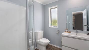 A bathroom with a glass shower enclosure, a white toilet, a window, and a sink with a mirror.