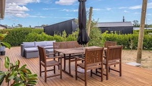 A wooden deck with a table and chairs, a grey sofa, and a black umbrella.