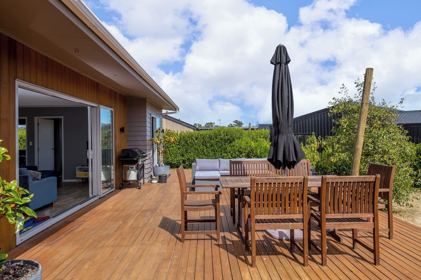 A wooden deck with outdoor furniture, a grill, and a covered umbrella.