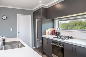 A modern kitchen with a built-in stove, refrigerator, and a window overlooking greenery.