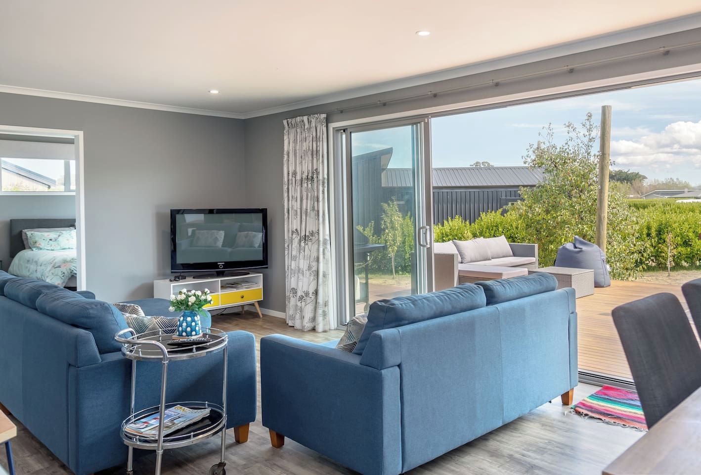 A modern living room with a flat-screen TV, a sofa set, and a dining area with outdoor seating.