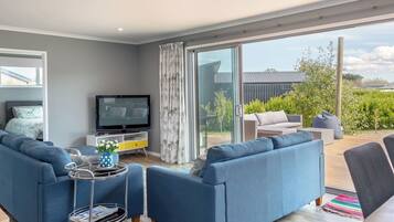 A modern living room with a flat-screen TV, a sofa set, and a dining area with outdoor seating.