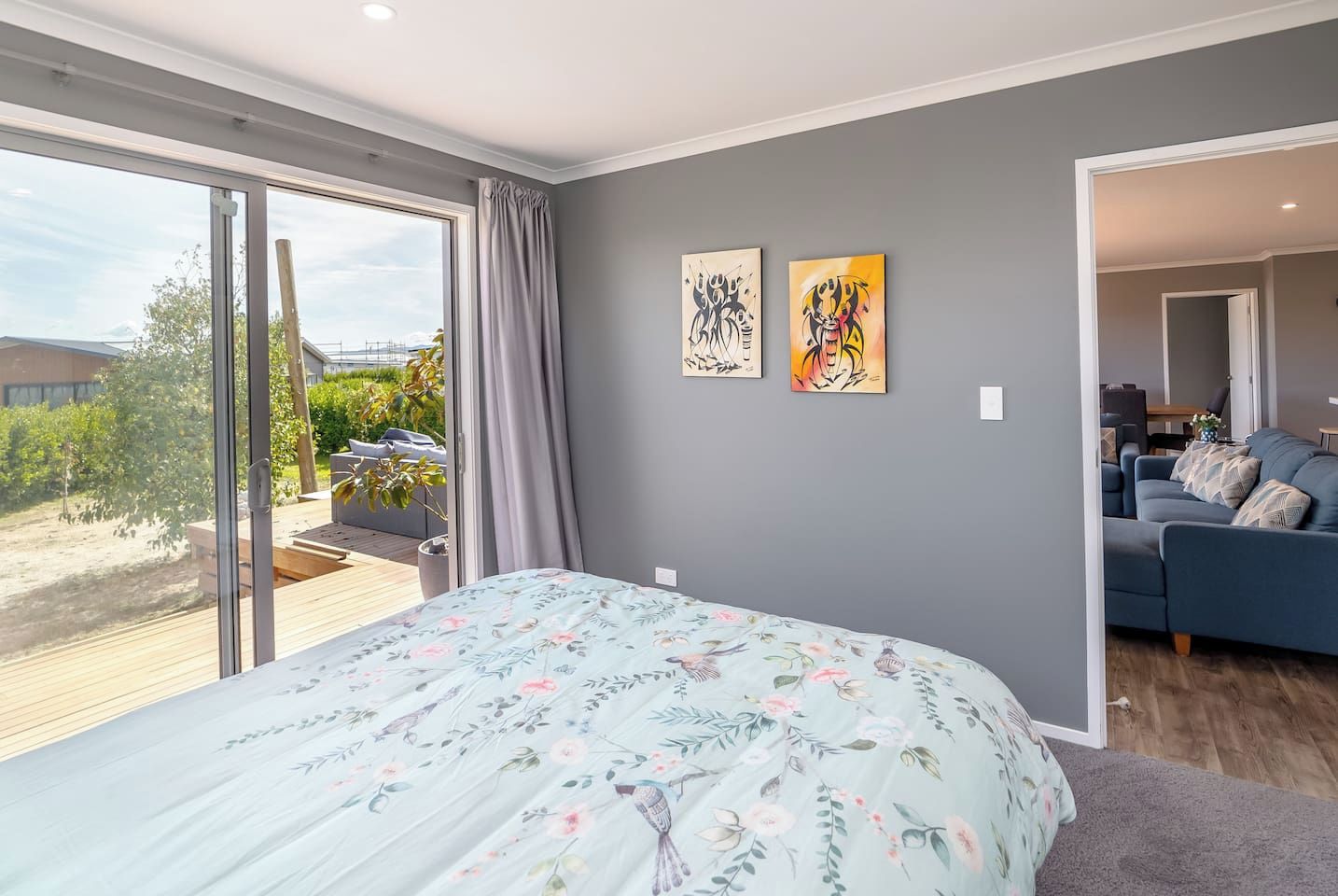 A bedroom with a large bed, a sliding glass door to a balcony, and two wall art pieces.