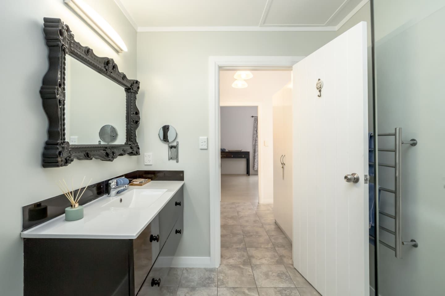 Une salle de bain avec un lavabo blanc, un meuble sombre, un miroir décoratif et un porte-serviettes.