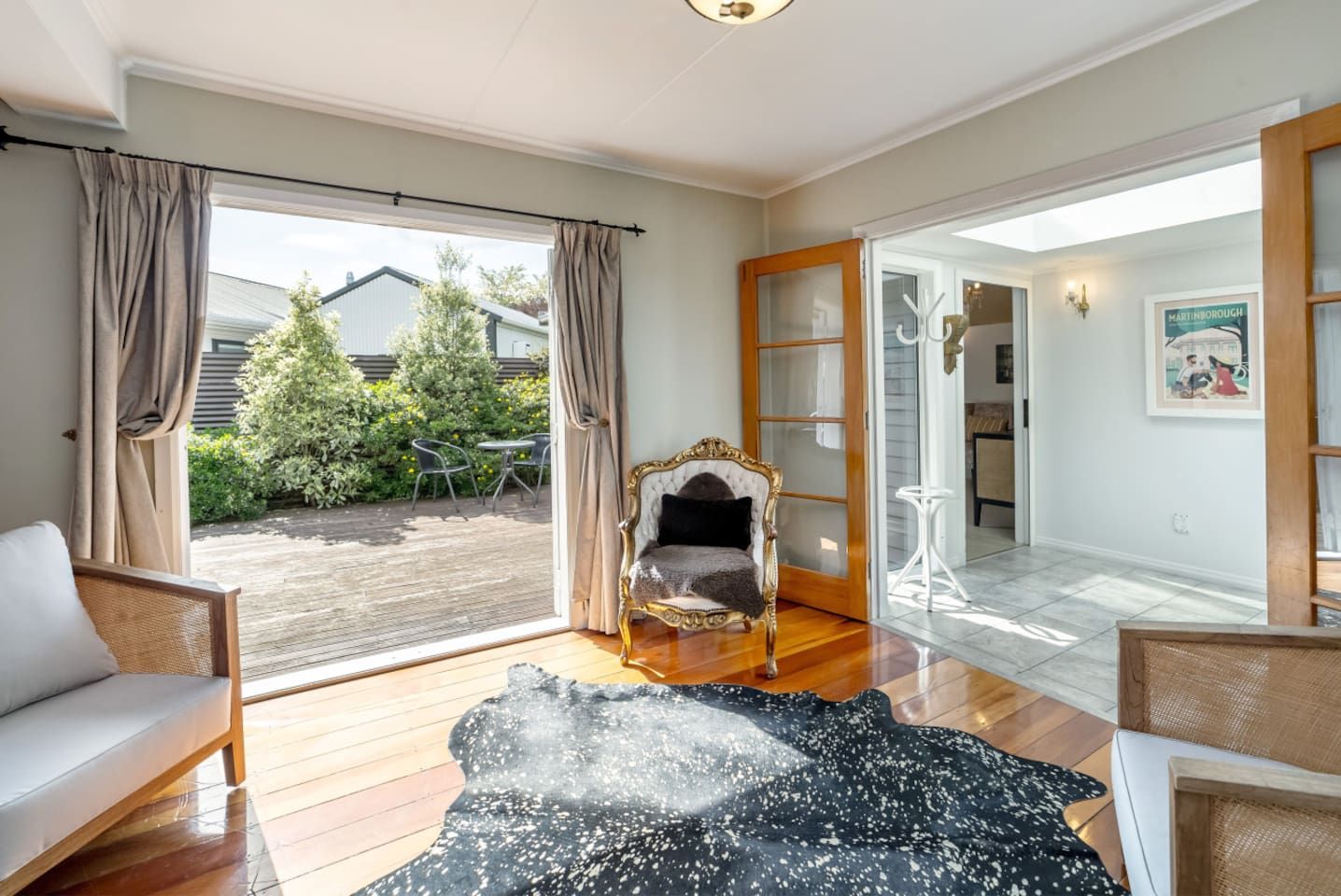 A spacious room with a large sliding glass door leading to a wooden deck, a plush sofa, a decorative chair, and a small table.