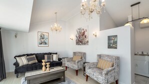 A modern living room with a black sofa, patterned armchairs, a wooden coffee table, and a chandelier. - Charming Character Retreat | 2BR, Private Deck & Year-Round Comfort (Martinborough)