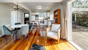 A spacious living room with a dining area, a kitchen, and a large sliding glass door leading to an outdoor deck. - Charming Character Retreat | 2BR, Private Deck & Year-Round Comfort (Martinborough)