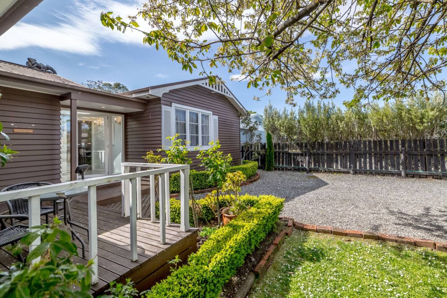 A residential property with a deck, a fenced backyard, and a gravel driveway.