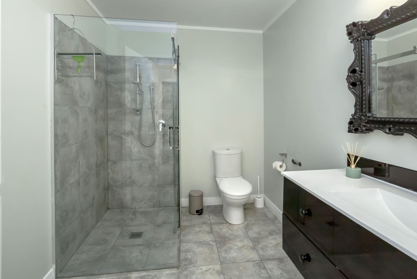 Un baño con ducha envuelta en vidrio, un inodoro blanco y un tocador oscuro con espejo.