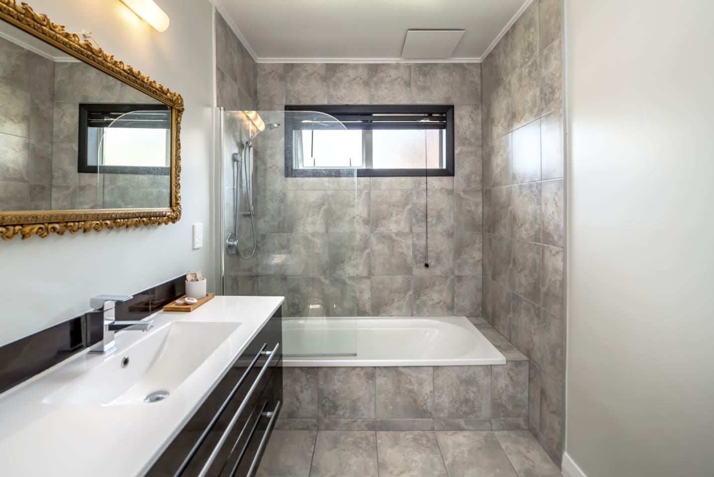 A modern bathroom with a double vanity, a freestanding bathtub, and a large mirror with a decorative frame.