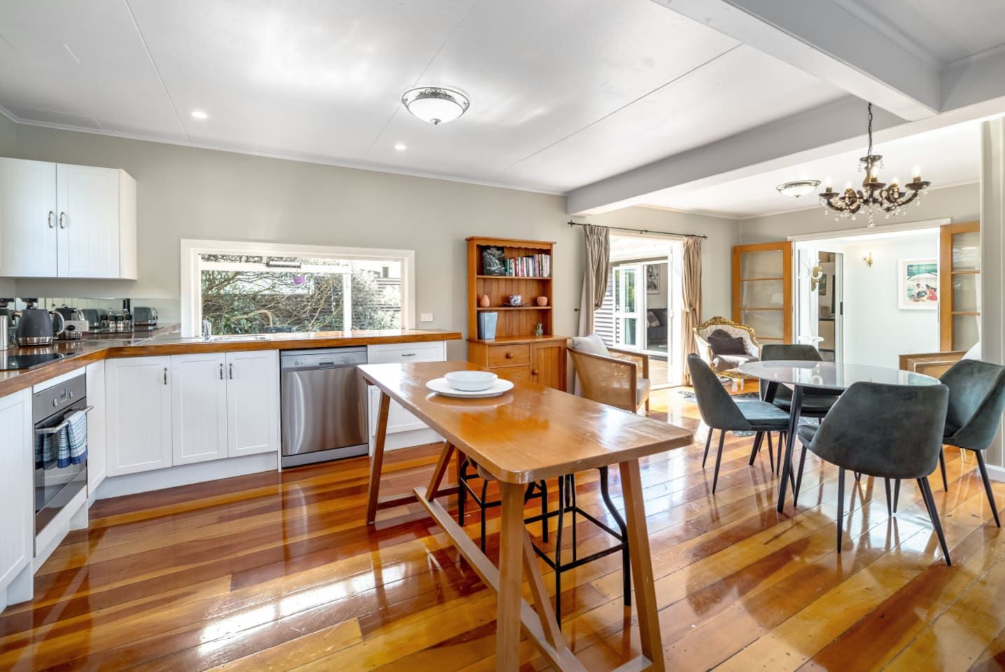 A modern kitchen with wooden flooring, white cabinetry, and a dining area with a table and chairs.