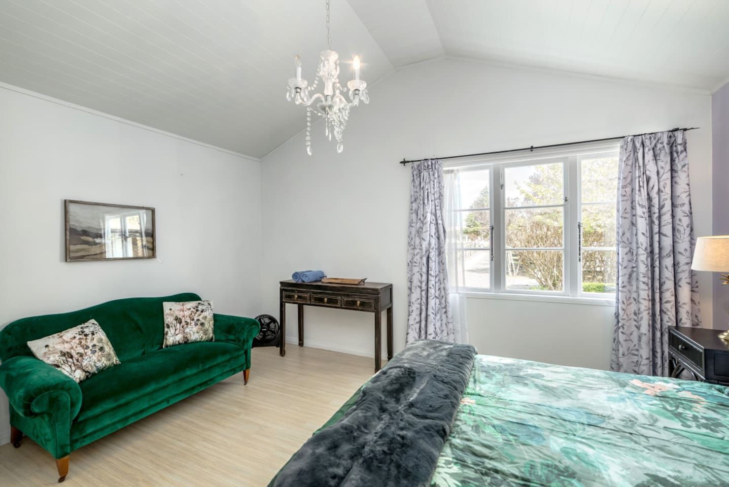 A room with a green sofa, a bed, a desk, and a window with curtains.