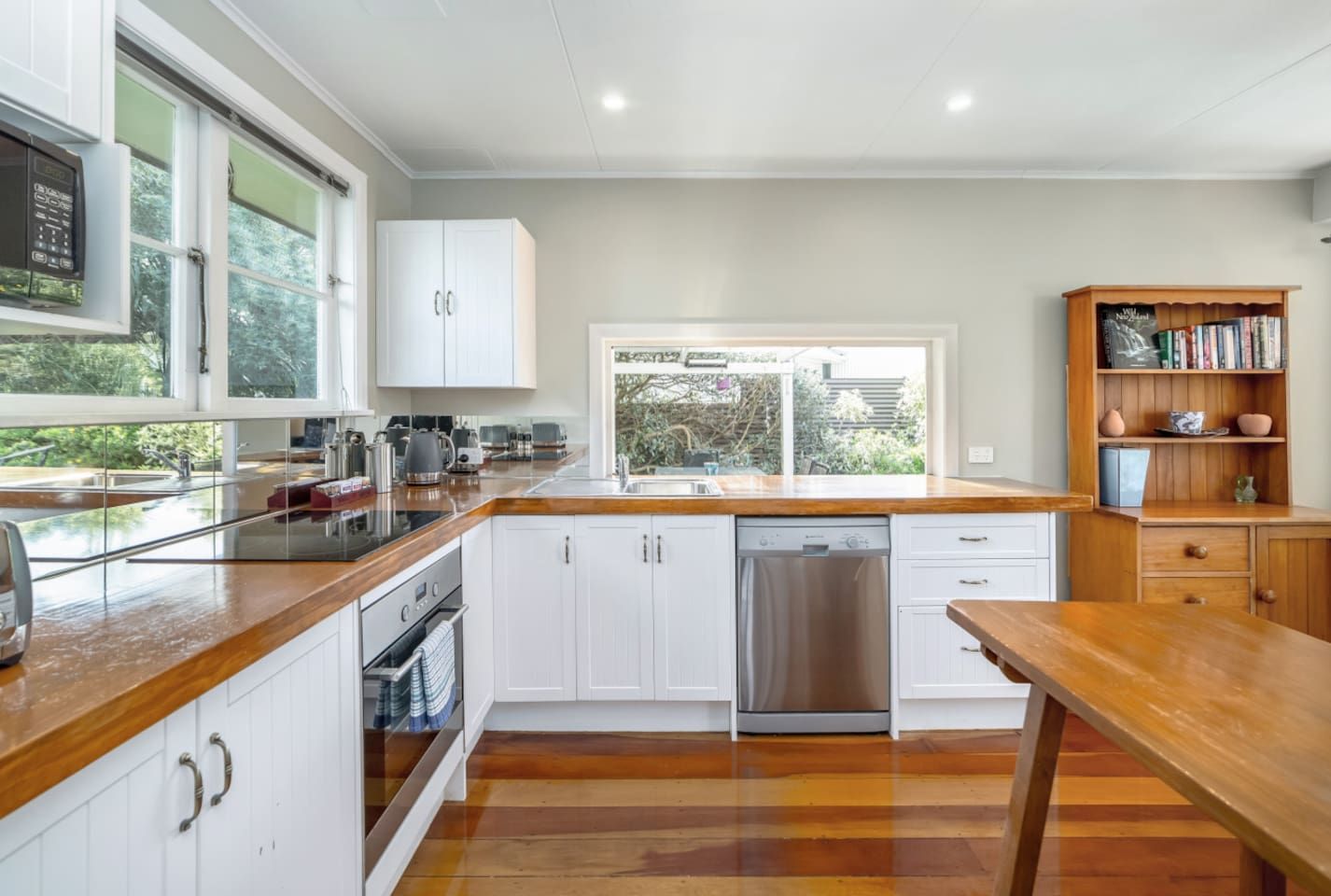 A modern kitchen with white cabinetry, a wooden countertop, and a view of the outdoors.