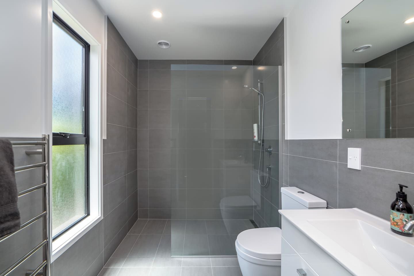 A modern bathroom with a glass shower enclosure, a toilet, and a sink with a soap dispenser.
