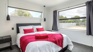 A bedroom with a bed, a nightstand, a window, and curtains. - Broadway On New York (Martinborough)
