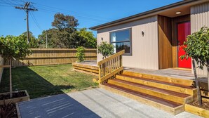 A modern single-story house with a red door, a wooden staircase, and a fenced backyard. - Broadway On New York (Martinborough)
