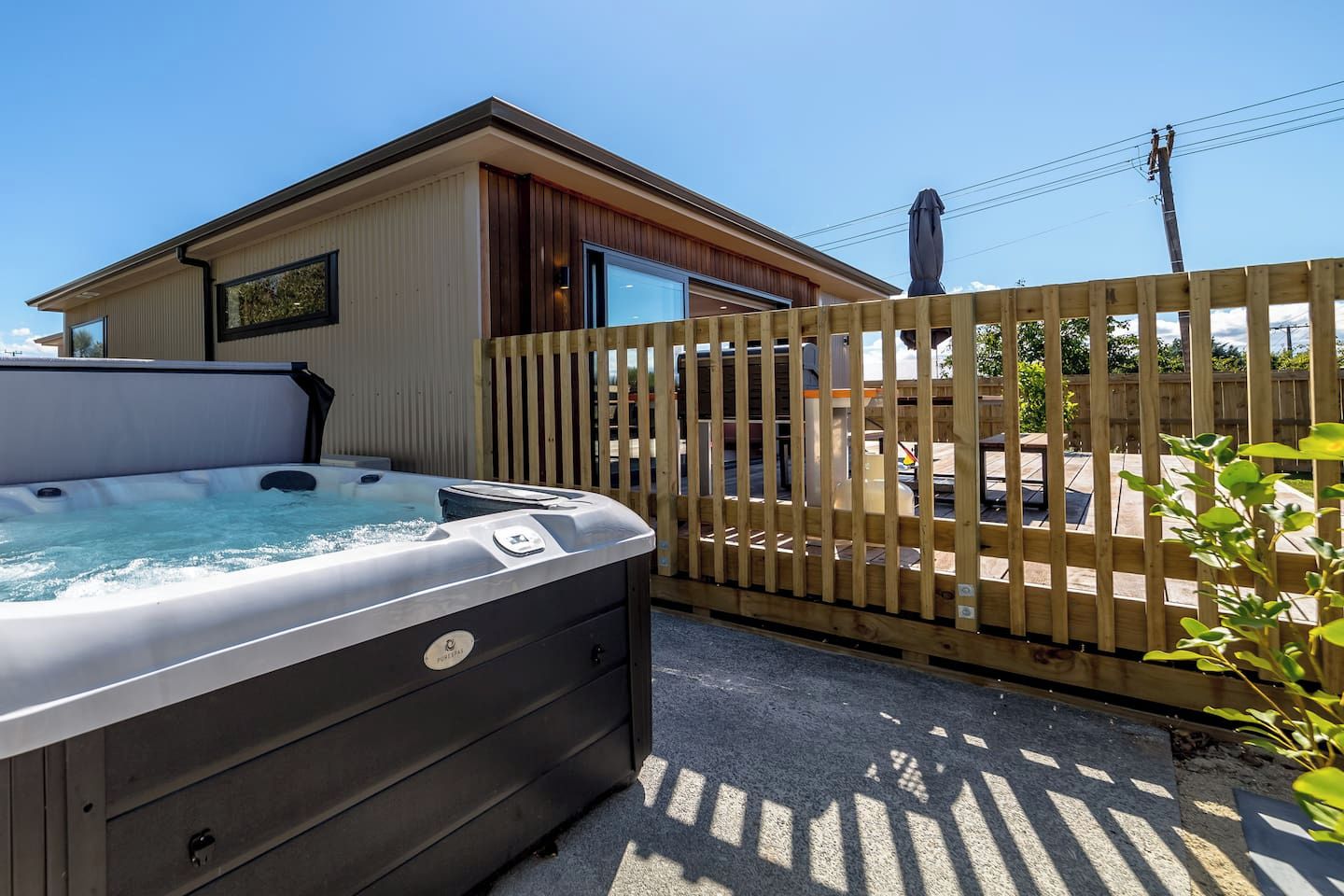A hot tub outside a building with a wooden fence, a clear sky, and a person on a utility pole.