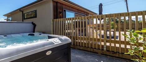 A hot tub outside a building with a wooden fence, a clear sky, and a person on a utility pole.