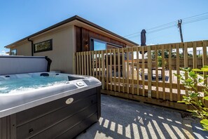 A hot tub outside a building with a wooden fence, a clear sky, and a person on a utility pole. - Broadway On New York (Martinborough)